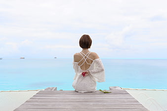 Woman in white dress sitting on pier facing turquoise ocean