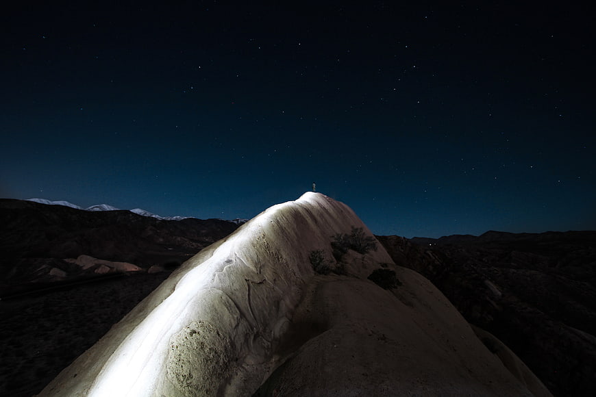 Lone figure standing on illuminated desert rock formation under starry night sky