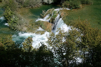 Aerial View of Turquoise Waterfall Cascading Through Lush Green Forest