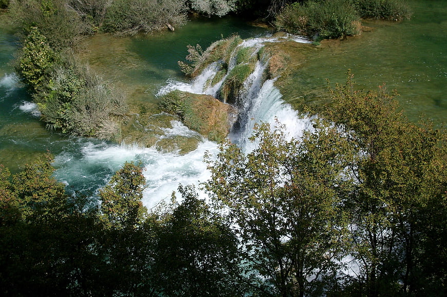 Aerial View of Turquoise Waterfall Cascading Through Lush Green Forest