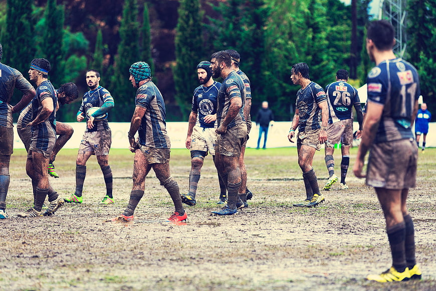 Muddy rugby players resting on field during match