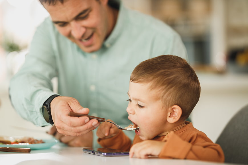 Father feeding toddler son breakfast at kitchen table