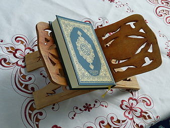 Quran on wooden stand with gold calligraphy on floral tablecloth