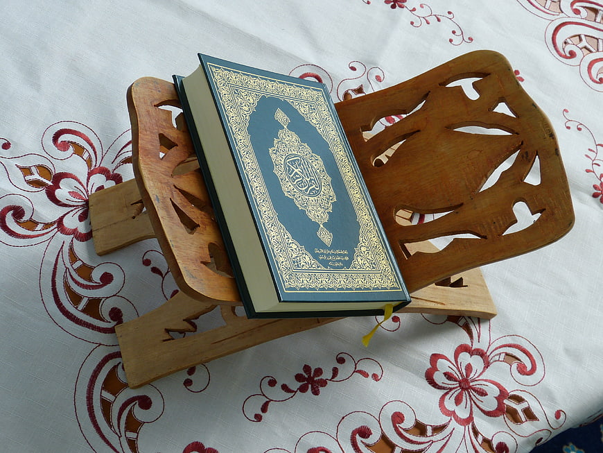 Quran on wooden stand with gold calligraphy on floral tablecloth
