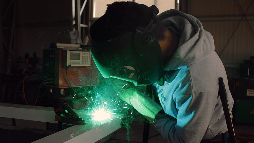 Welder in protective gear working with sparks in workshop