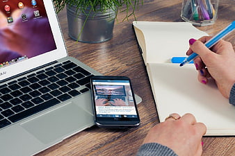 Woman writing in notebook with laptop and smartphone on desk