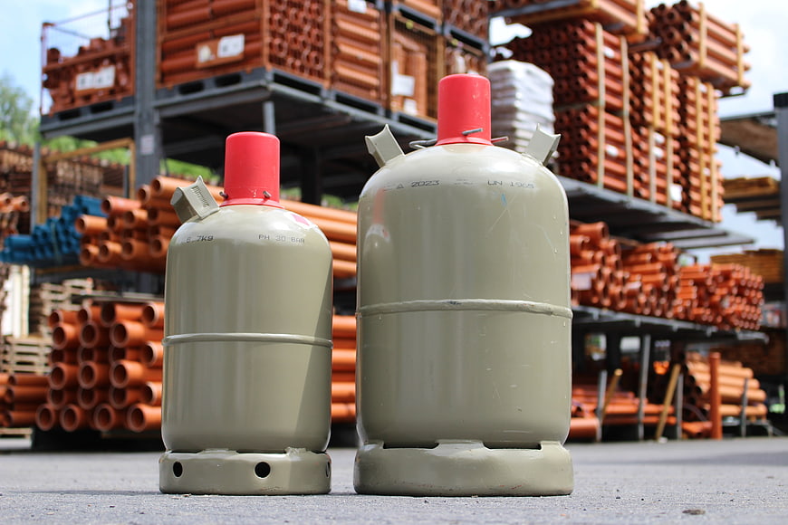 Two beige gas cylinders with red caps in an industrial yard
