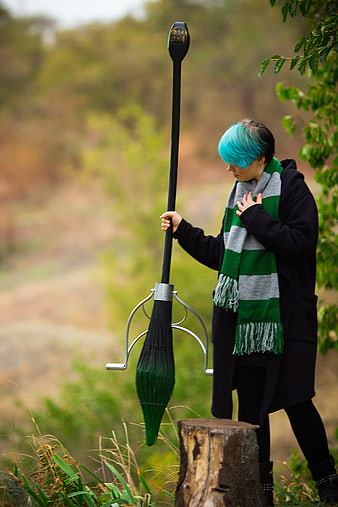Person with blue hair holding a broom in a forest