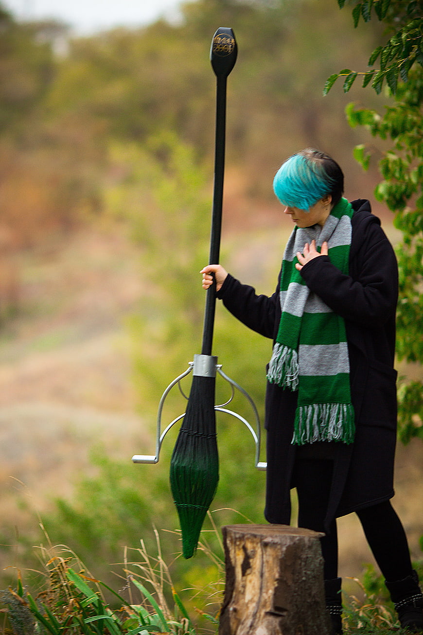 Person with blue hair holding a broom in a forest