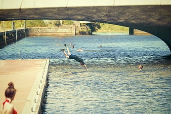 Man diving into river under bridge on summer day