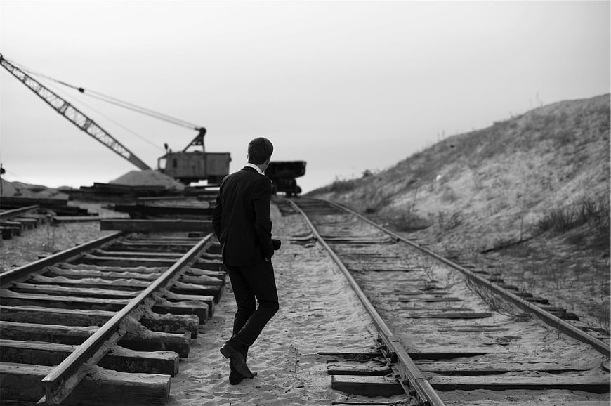 Man in Suit Walking on Railway Tracks in Black and White
