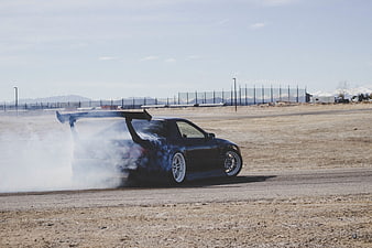 Black drift car performing burnout on desert track