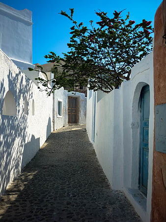 Narrow cobblestone alley in Santorini with white walls and blue sky