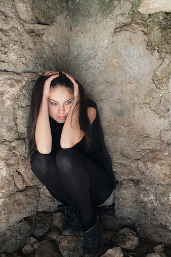 Sad woman in black crouching against stone wall