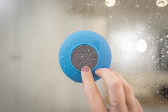 Hand pressing button on blue waterproof speaker in shower