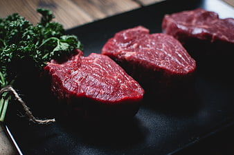 Raw beef steaks on black slate with fresh herbs
