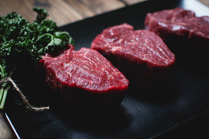 Raw beef steaks on black slate with fresh herbs