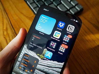 Hand holding iPhone with productivity app widgets on wooden desk