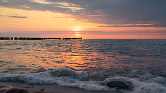 Sunset over Baltic Sea with wooden breakwater and waves