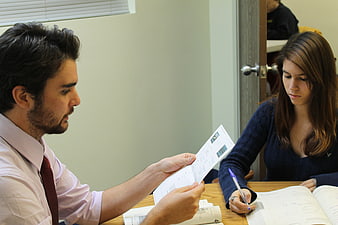 Male tutor explaining documents to female student at desk