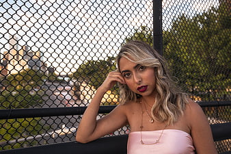 Stylish Blonde Woman in Pink Top Leaning on Fence