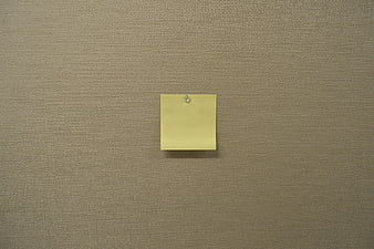 Blank yellow sticky note pinned to textured beige wall background