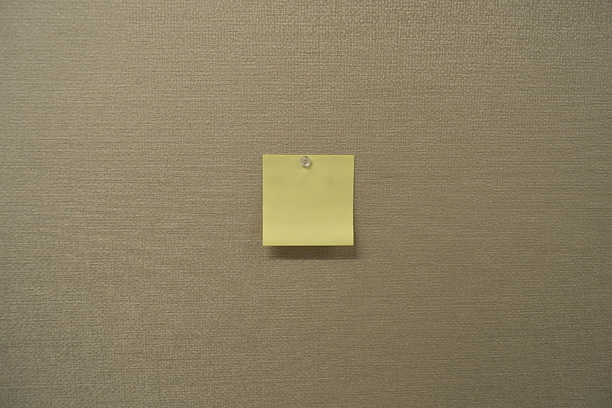 Blank yellow sticky note pinned to textured beige wall background