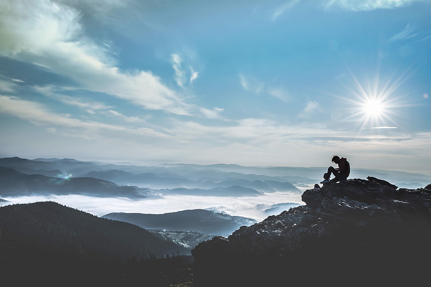 Silhouette of a hiker sitting on a mountain peak above a sea of clouds