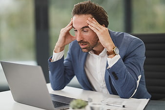 Stressed businessman holding head while working on laptop