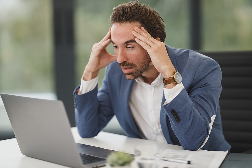 Stressed businessman holding head while working on laptop