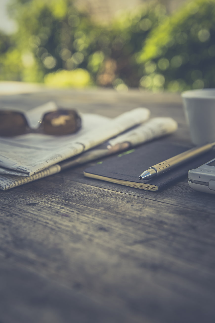Vintage workspace with newspaper, notebook, and pen on wooden table