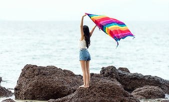 Young woman holding colorful flag on coastal rocks