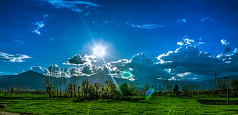 Vibrant Green Field with Mountains and Blue Sky