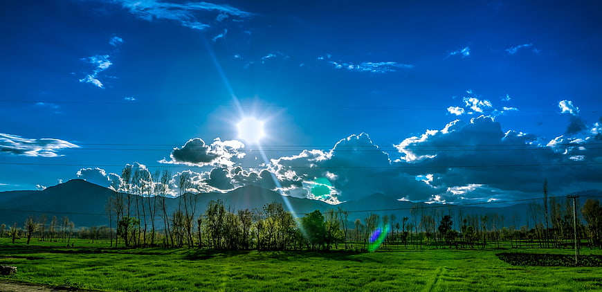 Vibrant Green Field with Mountains and Blue Sky