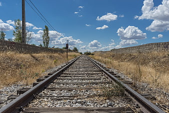 Railway tracks leading to horizon under blue sky