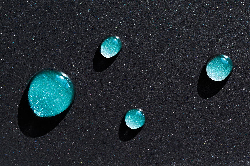 Glittering teal liquid drops on dark textured background
