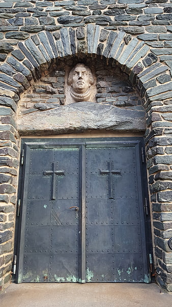 Old stone church entrance with carved bust and metal doors