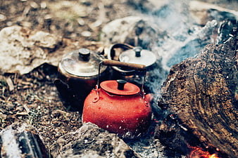 Red camping kettle boiling over rustic campfire