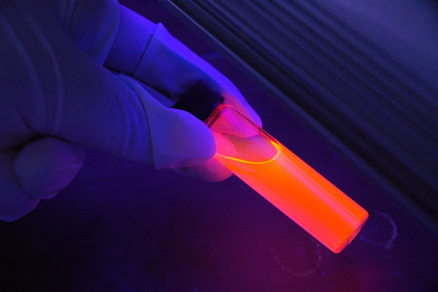 Gloved Hand Holding Glowing Orange Vial Under UV Light