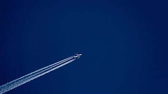Airplane with contrails flying in deep blue sky