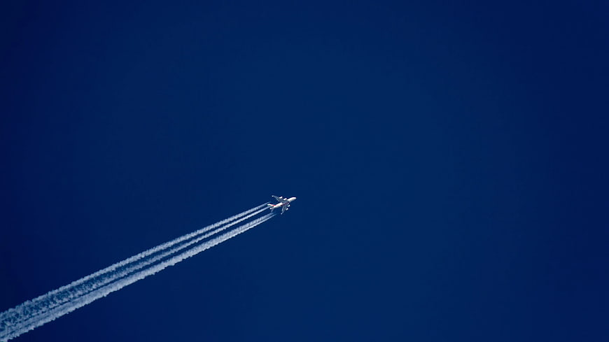 Airplane with contrails flying in deep blue sky