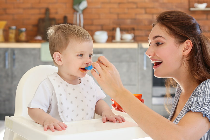 Happy Mother Feeding Toddler in High Chair