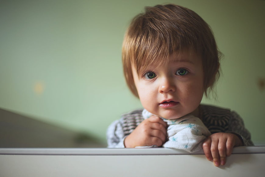 Cute Toddler Girl Looking Up While Leaning On White Bed Rail