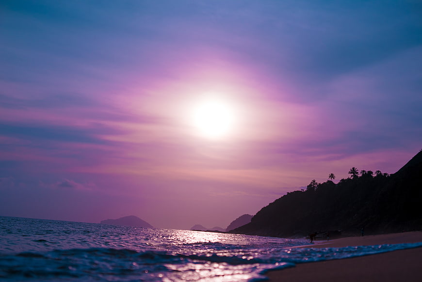Vibrant Purple Sunset Over Tropical Beach with Silhouette Hills