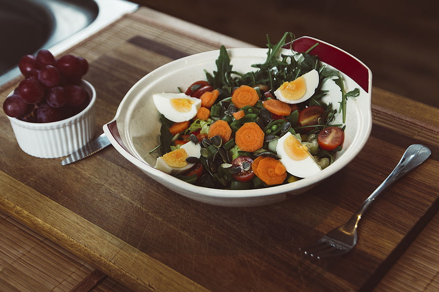 Healthy salad with eggs, carrots, and grapes on wooden board