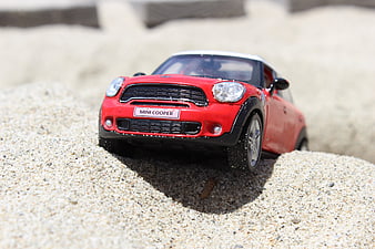 Red Mini Cooper toy car on sandy beach surface