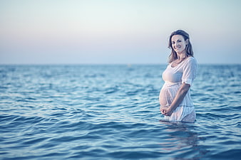 Pregnant woman in white dress standing in calm blue ocean water