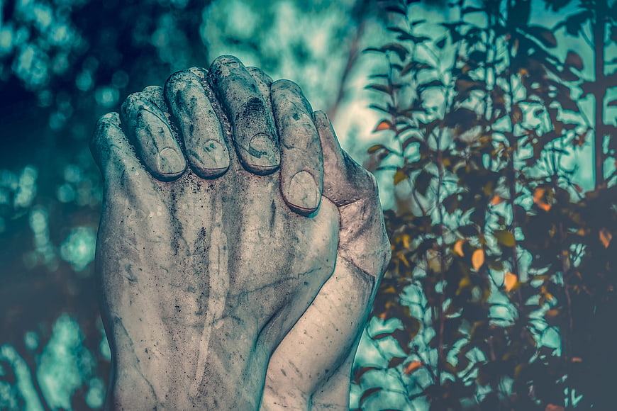 Close-up of weathered stone praying hands sculpture in a garden