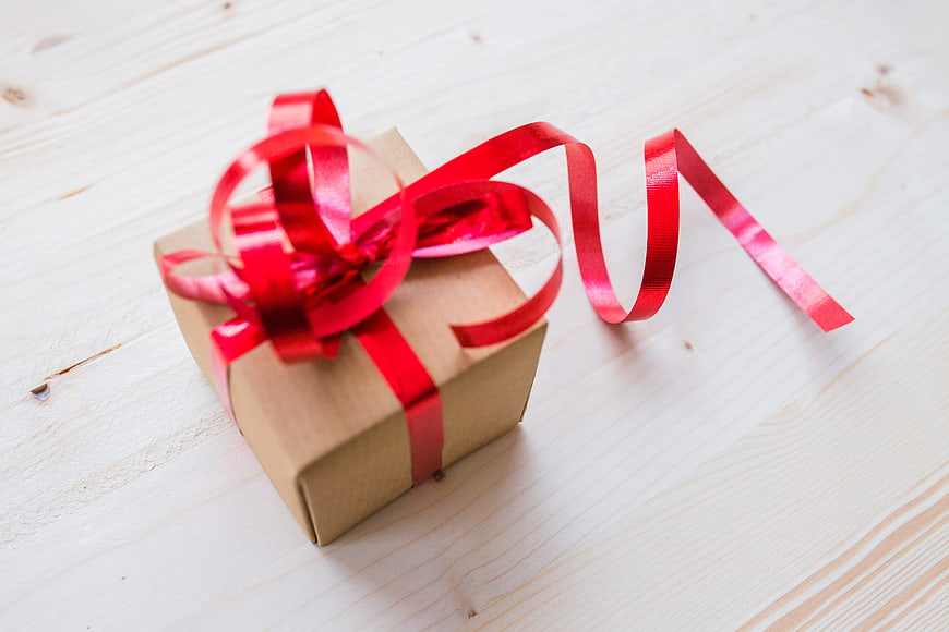 Small brown gift box with red ribbon on white wood