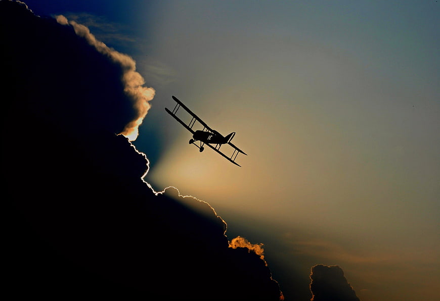 Silhouette of vintage biplane flying against dramatic sunset clouds
